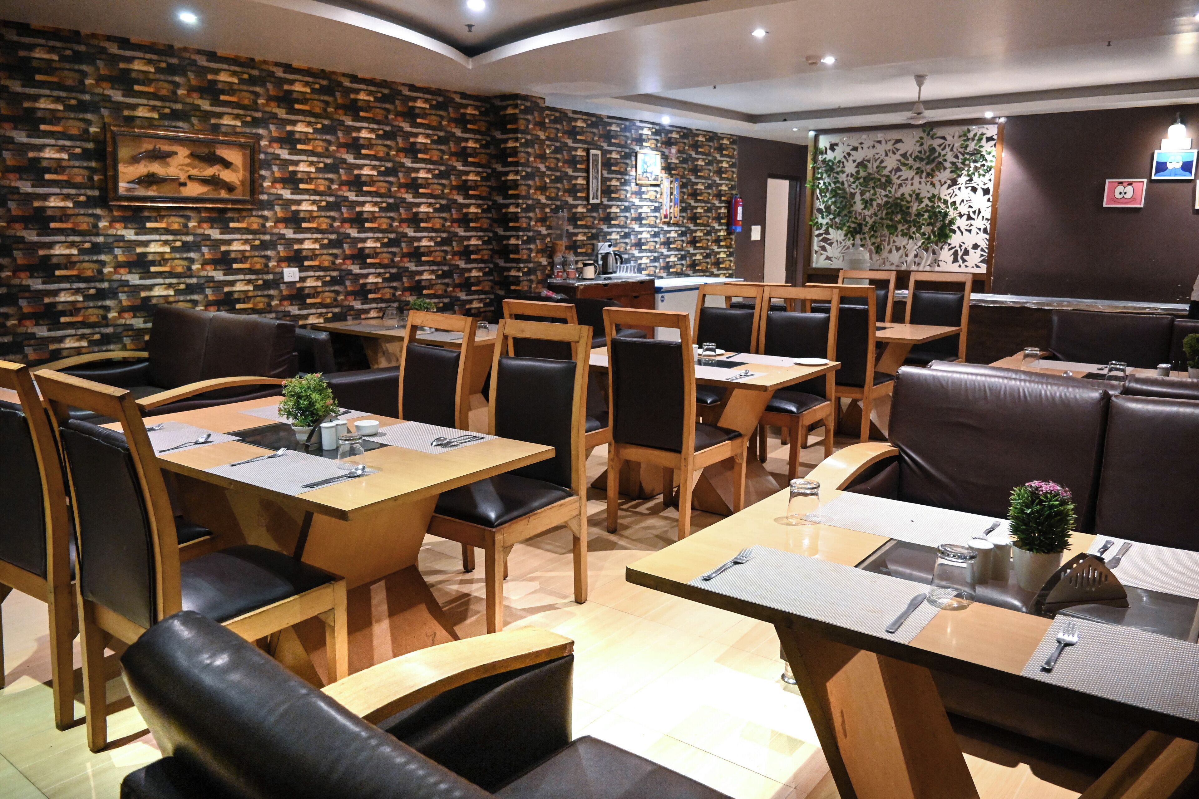 A restaurant with wooden tables and black leather chairs, a stone wall, and a small plant on the tables.