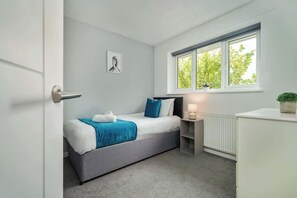 A bedroom with a bed, bedside table, and a window with a view of trees.