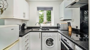 Una cocina compacta con armarios blancos, lavadora integrada, microondas y pileta.
