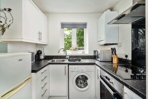Eine kleine Küche mit weißen Schränken, einer eingebauten Waschmaschine, einer Mikrowelle und einem Spülbecken.