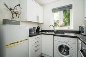 Eine kompakte Küche mit weißen Schränken, einer integrierten Waschmaschine und einem Fenster mit Blick auf Grünflächen.