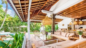 Amplia zona de estar al aire libre con piscina, muebles de madera y plantas tropicales.