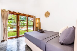 Une chambre à coucher avec un lit, une vue sur un jardin et une porte donnant sur l’extérieur.