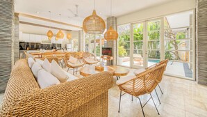 A spacious living area with wicker furniture, a dining set, and large windows offering a view of the outdoors.