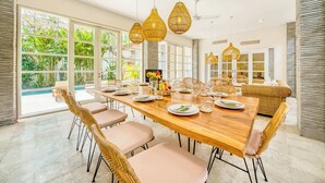 A dining area with a long wooden table, wicker chairs, and hanging pendant lights.