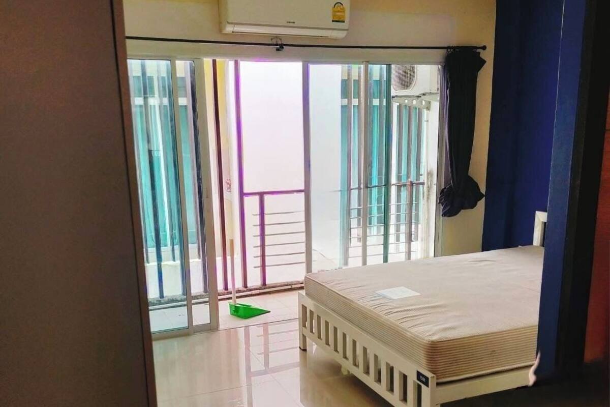 A bedroom with a bed, an air conditioning unit, a sliding glass door leading to a balcony, and a tiled floor.