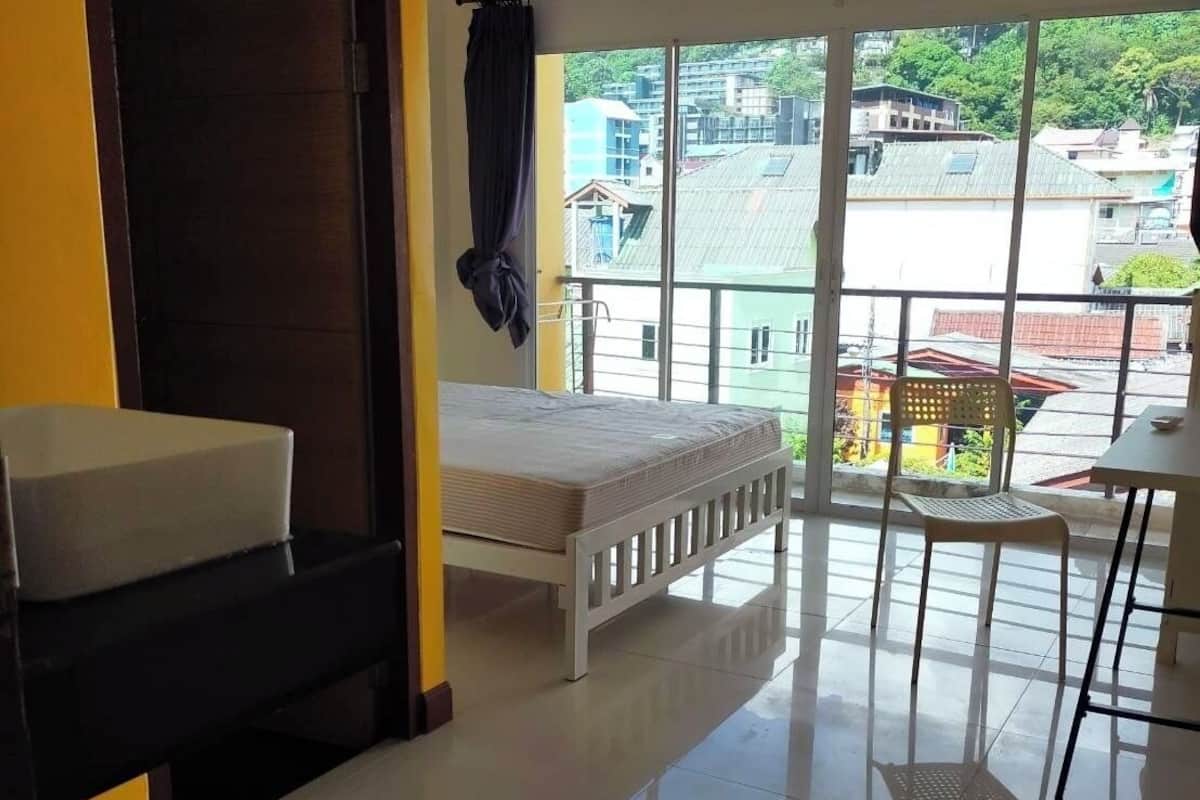A room with a bed, a small table, a chair, and a view of the city through large windows.
