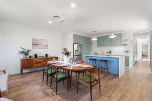 Uma cozinha moderna com ilha central, mesa de jantar de madeira e cadeiras estofadas em verde.