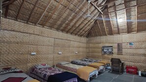 Ένα δωμάτιο με σκεπή από καλάμια, πολλά κρεβάτια με κουβέρτες, ένα μικρό τραπέζι και μια καρέκλα.