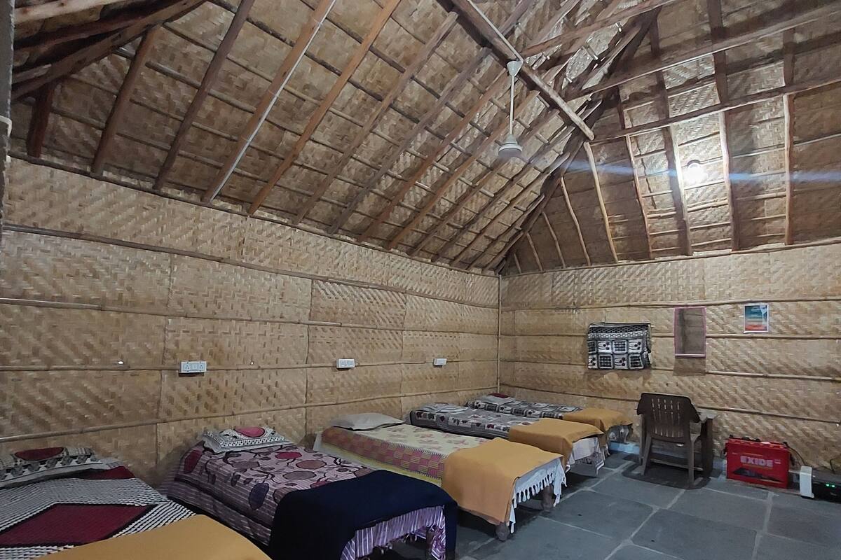 A room with thatched ceilings, multiple beds with blankets, a small table, and a chair.
