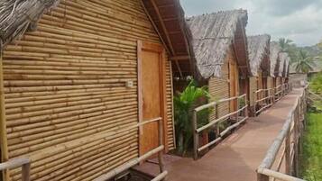 Un hilera de cabañas de madera con techo de paja, separadas por una pasarela de hormigón.