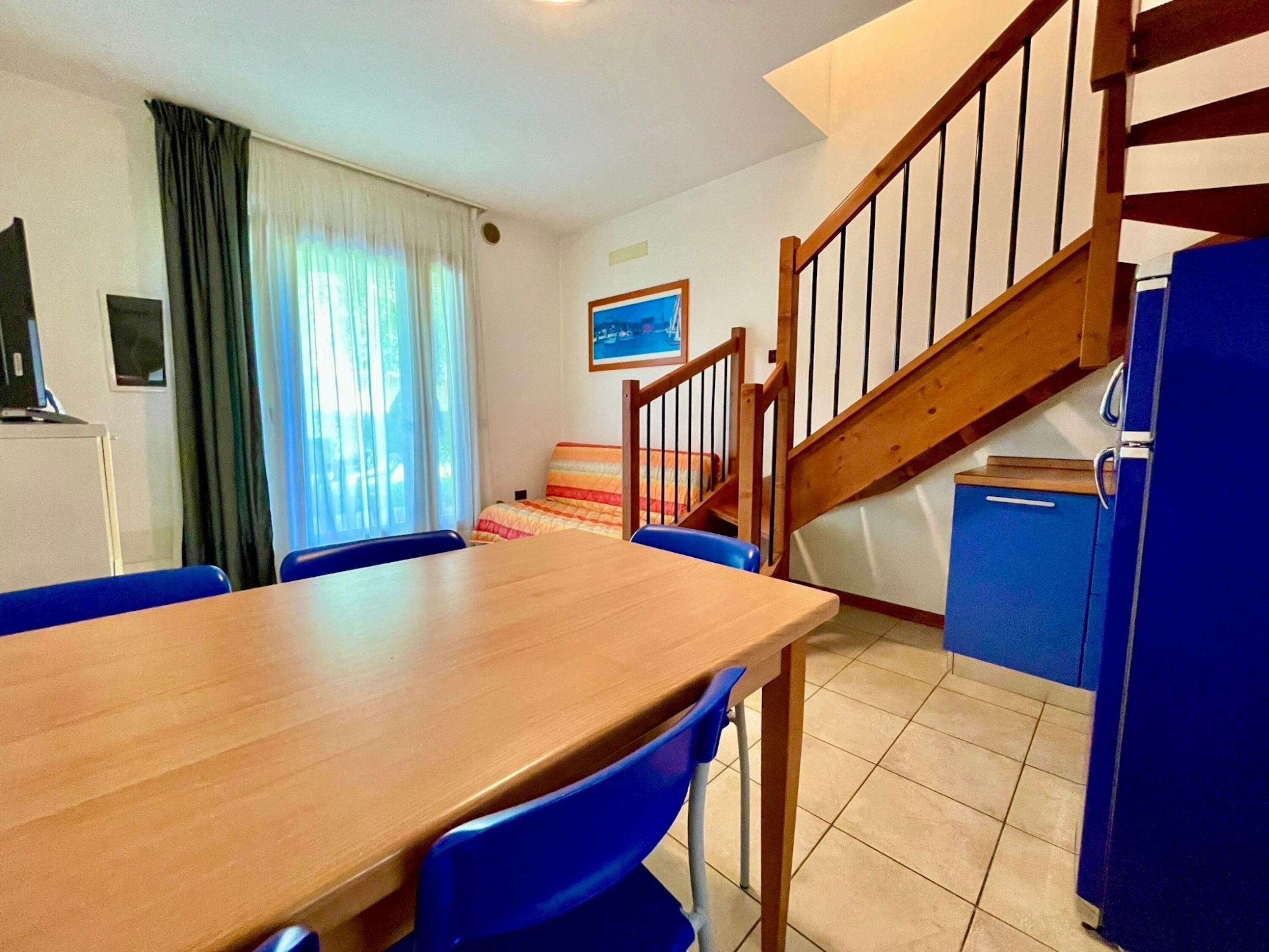 A dining area with a wooden table and blue chairs, a staircase, and a blue cabinet.