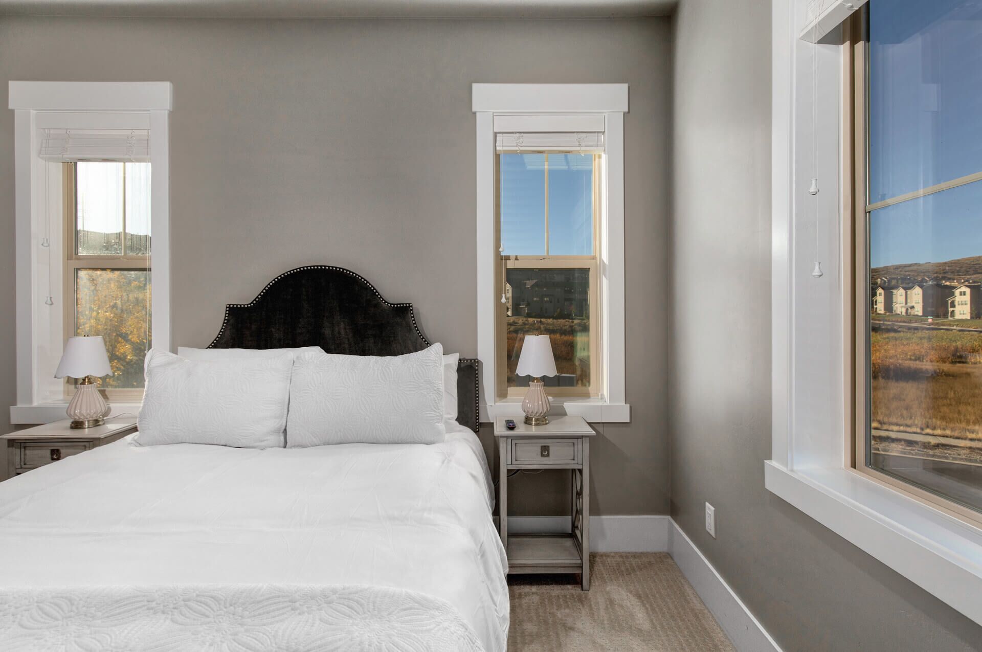 A bedroom with a bed, two bedside tables, a nightstand, and a large window with a view of buildings.