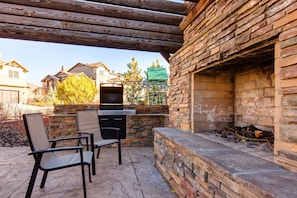 Un patio exterior con muros de piedra, una parrilla y sillas.