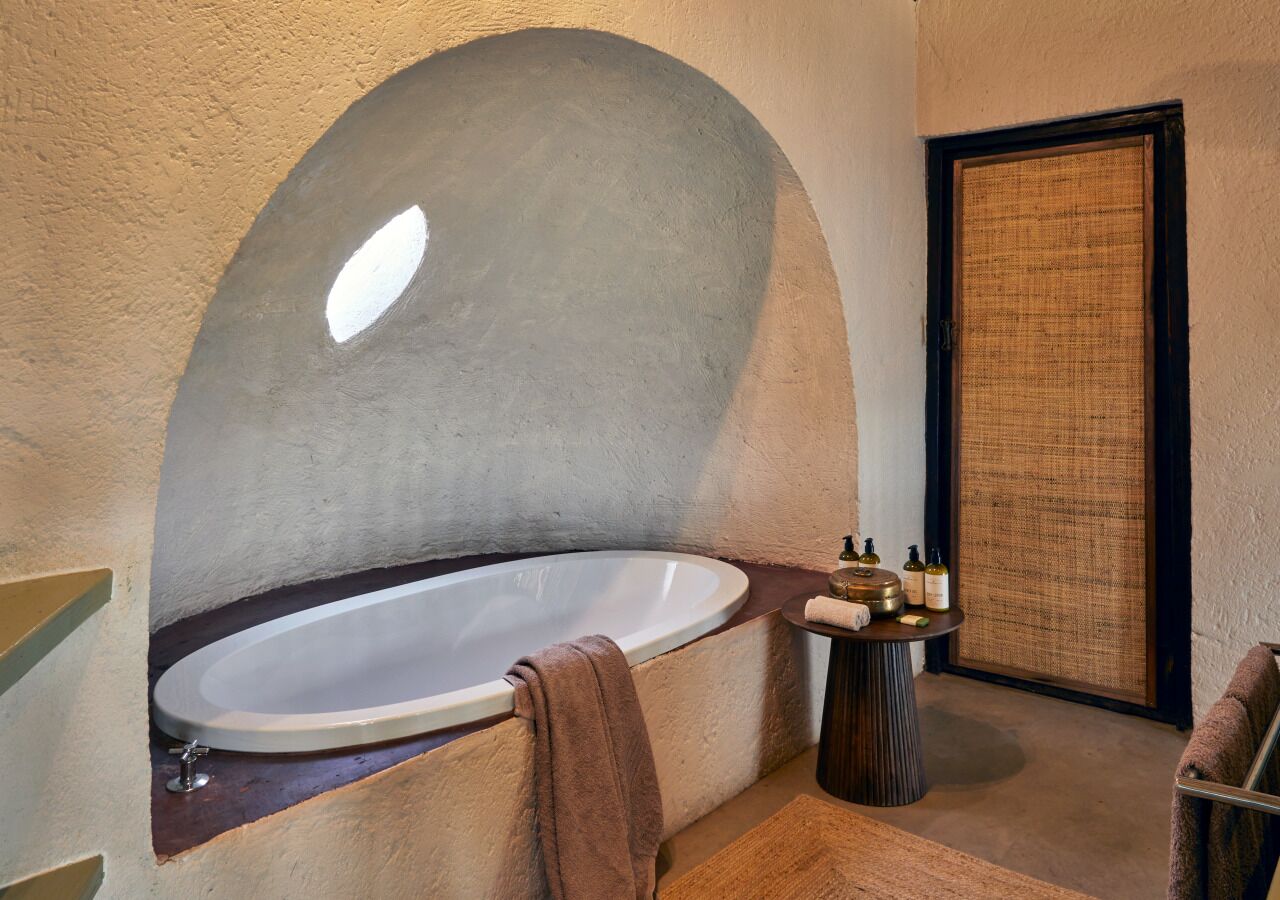 A modern bathroom with a freestanding bathtub, a small round table with toiletries, and a towel rack.