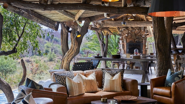 A cozy outdoor seating area with leather sofas and chairs, a coffee table, and a stone fireplace. - Toro River by Newmark (Makalali Game Reserve)
