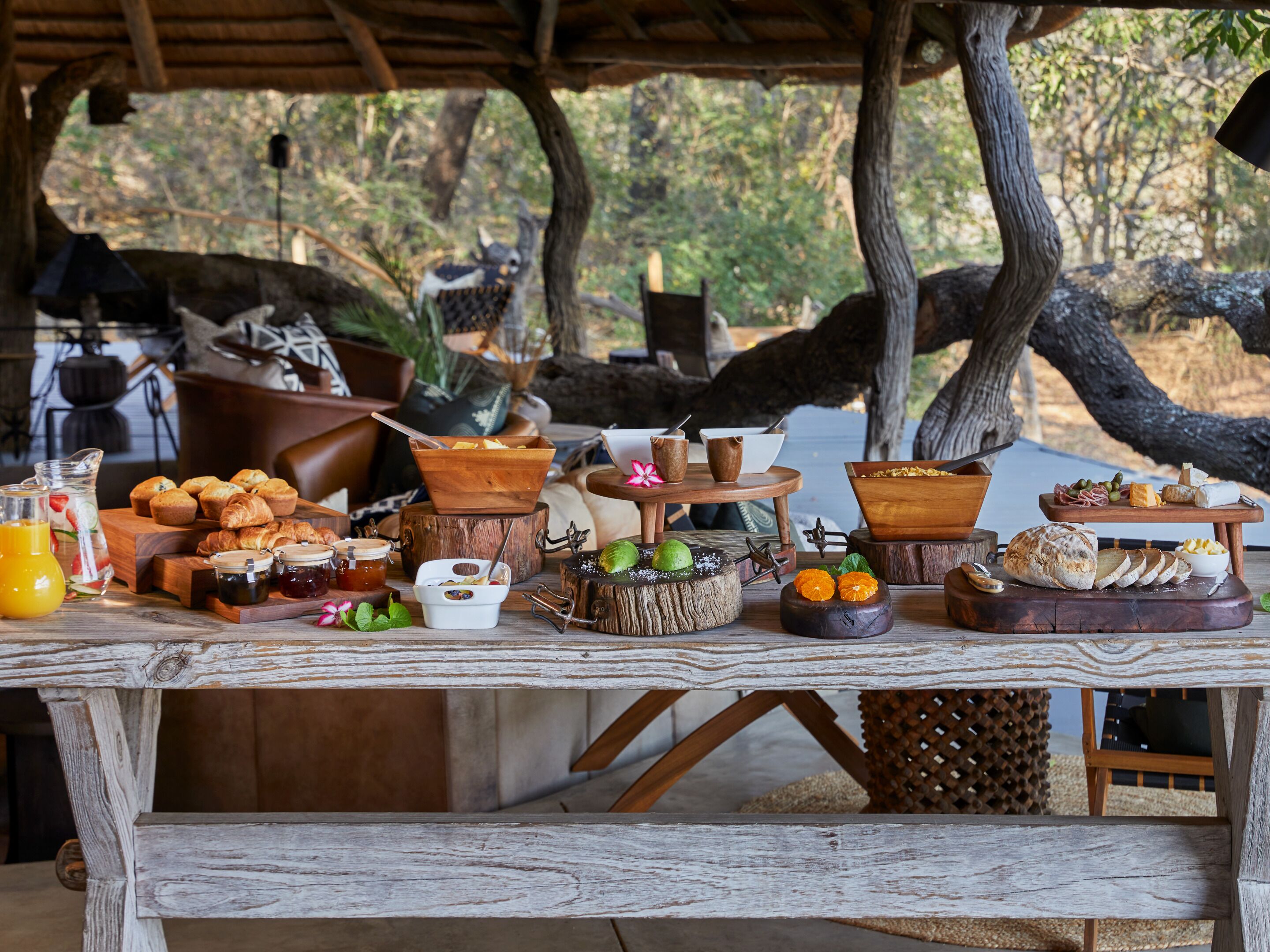 A rustic outdoor breakfast setup with various food items and beverages on a wooden table.