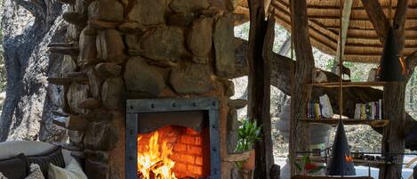 A stone fireplace with a fire, surrounded by seating and bookshelves.