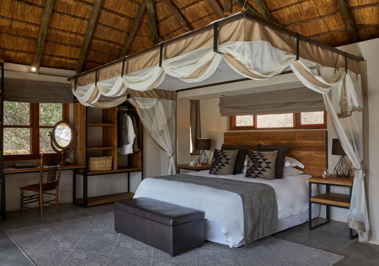 A bedroom with a canopy bed, a desk with a chair, and a large window.