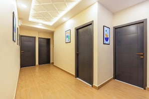 Un pasillo con tres puertas oscuras, suelo de madera e iluminación empotrada en el techo.