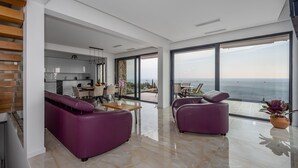 A modern living room with a large window, a kitchen, and a dining area.