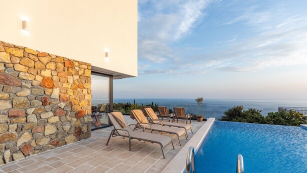 A pool area with a stone wall, lounge chairs, and a view of the sea.