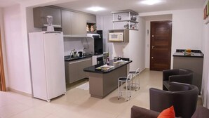 Eine kompakte Küche mit Kühlschrank, Mikrowelle und Herd. Ein kleiner Essbereich mit Tisch und zwei Stühlen ist ebenfalls vorhanden.