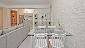 Una sala de estar moderna con una mesa de comedor de vidrio, sillas blancas, un sofá gris y una pared decorativa de ladrillo.