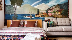 A bedroom with a bed, a sofa, and a large mural of a coastal scene. - Transylvanian Home - Mountain View, BBQ & Pool (Bratca)