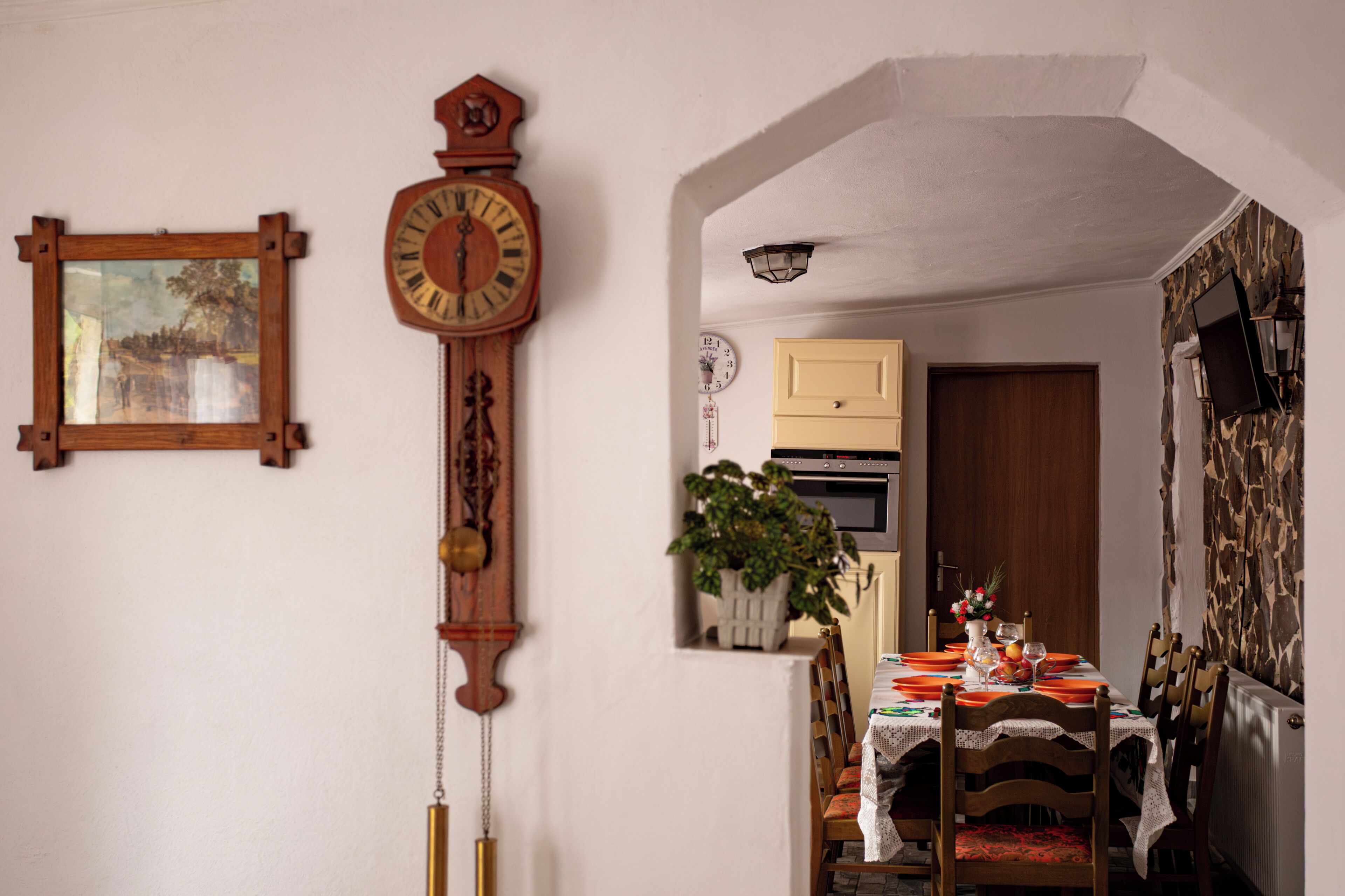 Comedor con mesa de madera dispuesta para dos personas, un reloj y una planta en maceta.