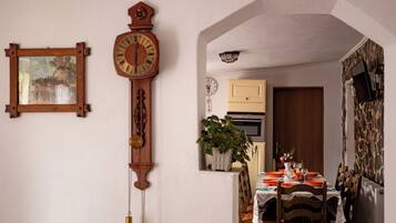Comedor con mesa de madera dispuesta para dos personas, un reloj y una planta en maceta.