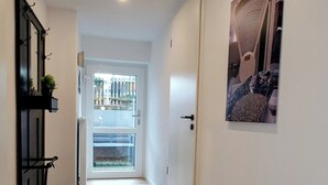 Un couloir doté d’un plancher en bois, une porte donnant sur un balcon et un tableau encadré accroché au mur.