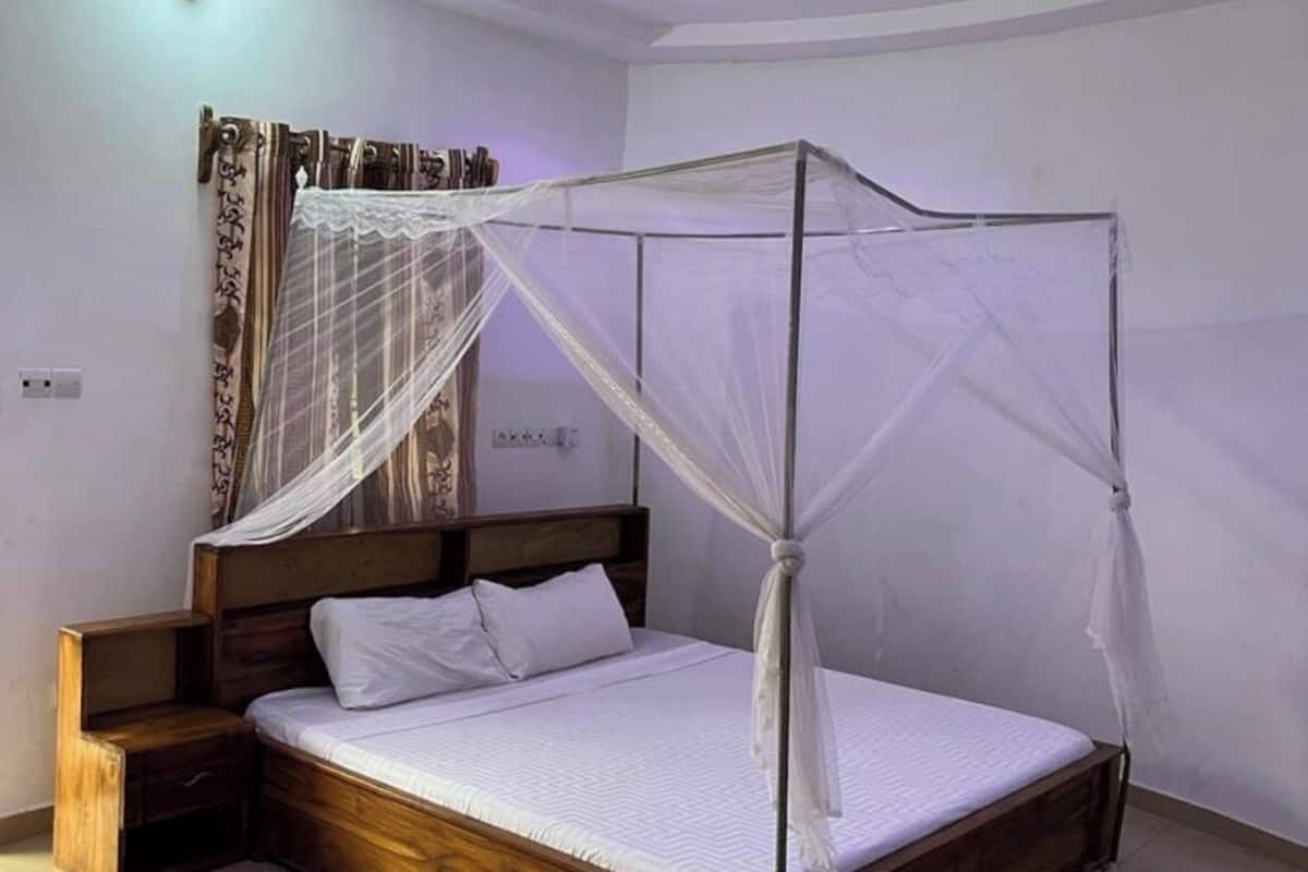 Un dormitorio con una cama de madera, una mesita de noche, un ventilador de techo y una ventana con cortinas.