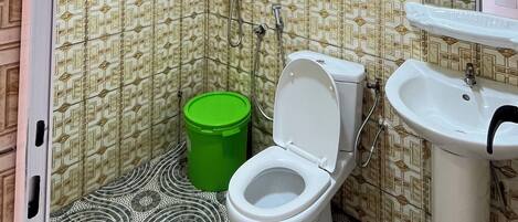 A bathroom with patterned wallpaper, a toilet, a green bucket, a shower, and a sink.