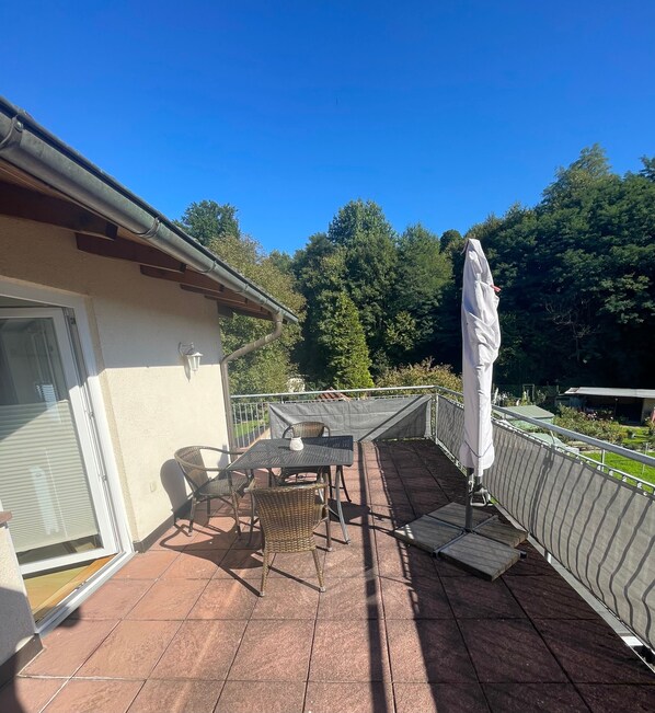 Une terrasse couverte avec une table et des chaises, un parasol blanc et une clôture en métal.