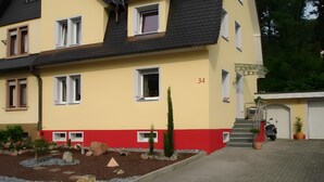 Un edificio de varios pisos con fachada roja y amarilla, número 34, que cuenta con una escalera, un garaje y un camino de acceso pavimentado.
