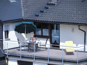 Ein Balkon mit Metallgeländer, einem Tisch mit Stühlen und einem gelb gestreiften Sessel.