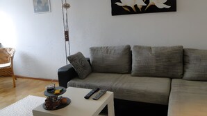 Una sala de estar con un sofá gris, una mesa de centro blanca, una lámpara de pie y un cuadro floral en blanco y negro en la pared.