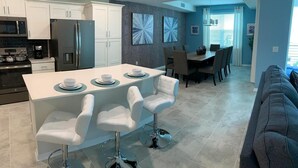 A modern kitchen with white cabinets, stainless steel appliances, and a central island with bar stools. - To Infinity And Beyond Storey Lake Resort By Shine Villas 2 Bedroom Condo (Kissimmee)