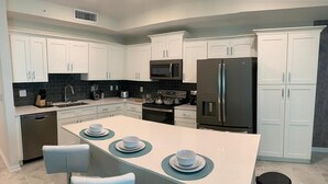 A modern kitchen with white cabinets, a central island with bar stools, stainless steel appliances, and a dishwasher. - To Infinity And Beyond Storey Lake Resort By Shine Villas 2 Bedroom Condo (Kissimmee)