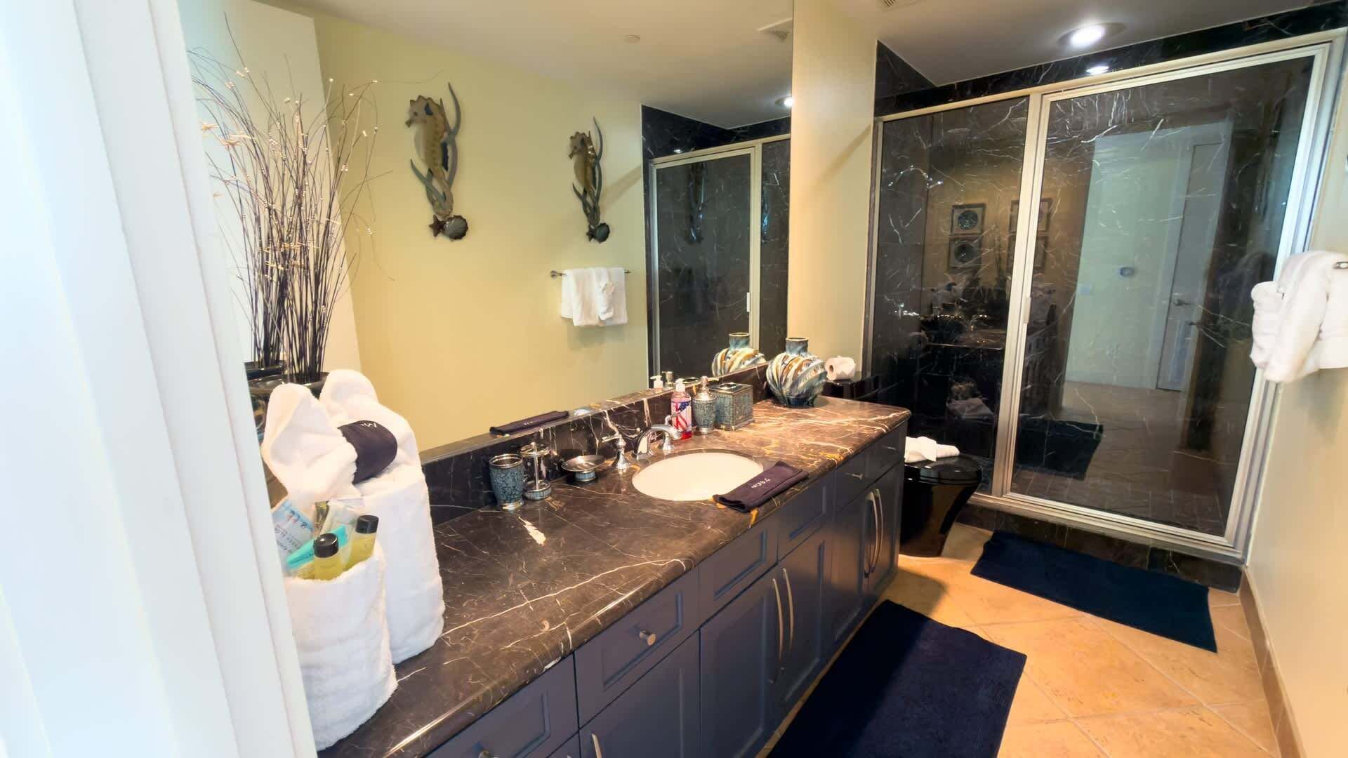 Un baño moderno con tocador de mármol, un espejo grande y cabina de ducha de vidrio.