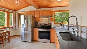 A modern kitchen with wooden cabinets, stainless steel appliances, and a large window providing a view of greenery. - Your Quiet Mountain Escape (Boone)