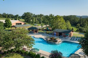 Une piscine avec des chaises longues et un kiosque, entourée d’arbres et d’un bâtiment.