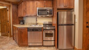 Una cocina con gabinetes de madera y electrodomésticos de acero inoxidable, incluyendo microondas, estufa, horno y refrigerador.