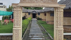 Una entrada con un portón ornamentado que da a un edificio con techo de paja.