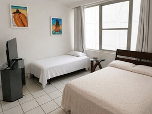 Quarto de hotel com duas camas de solteiro, televisão, uma mesinha e obras de arte nas paredes.