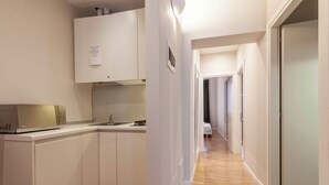 A modern kitchen with white cabinets, a microwave, and a sink. A hallway leads to a bedroom with a bed and a door. - San Polo Apartment with Balcony  (Venice)