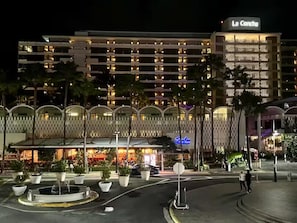Um hotel de vários andares com fachada moderna, um letreiro em destaque com a inscrição "La Concha" e um pátio ajardinado com plantas em vasos.