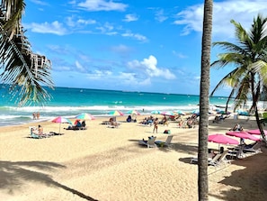 Uma praia com espreguiçadeiras, guarda-sóis, palmeiras e o oceano.