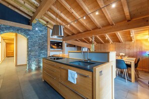 A modern kitchen with a stone wall, wooden beams, and a large island with a sink.
